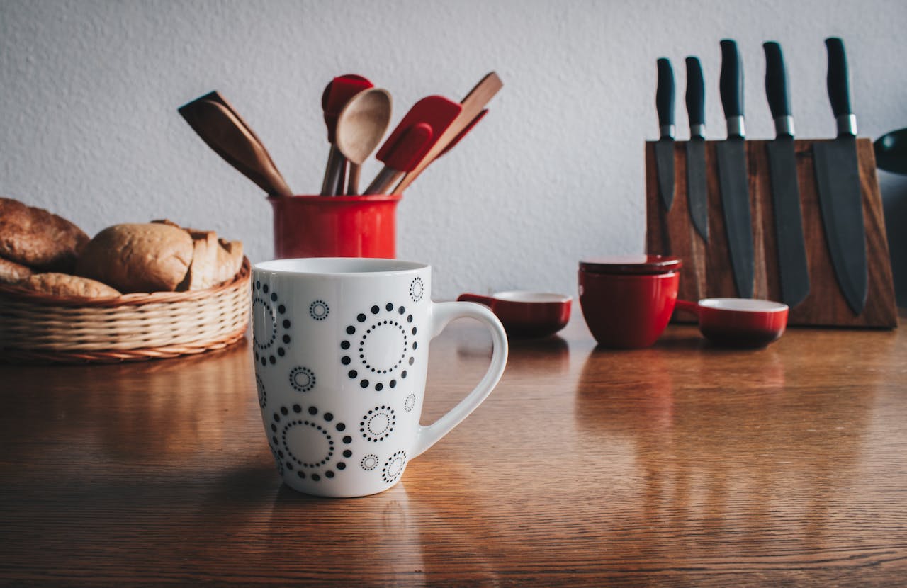 A cozy kitchen scene featuring a decorative mug, cutlery set, and fresh bread basket on a wooden table.